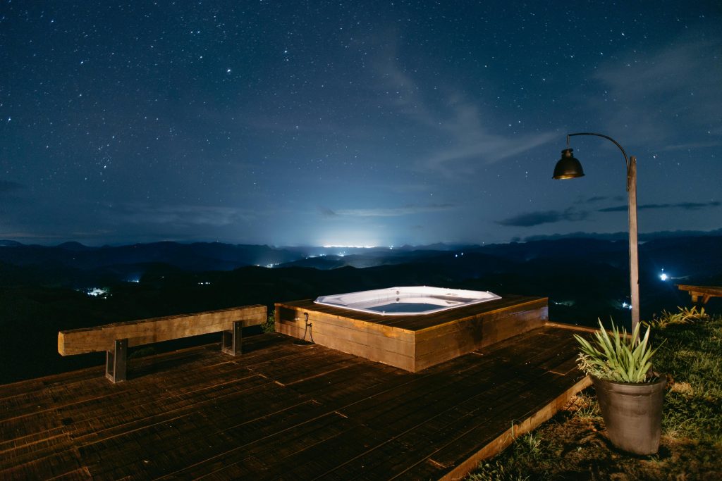 Relaxing outdoor jacuzzi under a starry sky with distant city lights in Santa Teresa, Brazil.